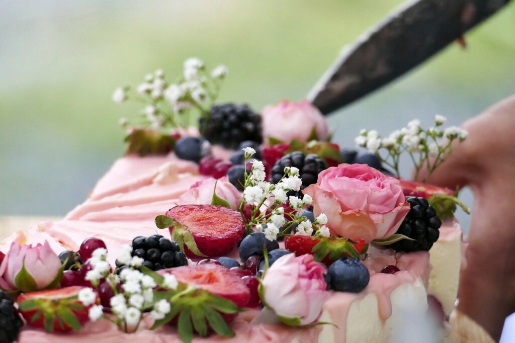 En kniv skjærer en dekorert kake toppet med rosa blomster, bjørnebær, bringebær, blåbær og jordbær – dens skjønnhet symboliserer tilliten til arbeidsplassen (tillit i arbeidslivet).