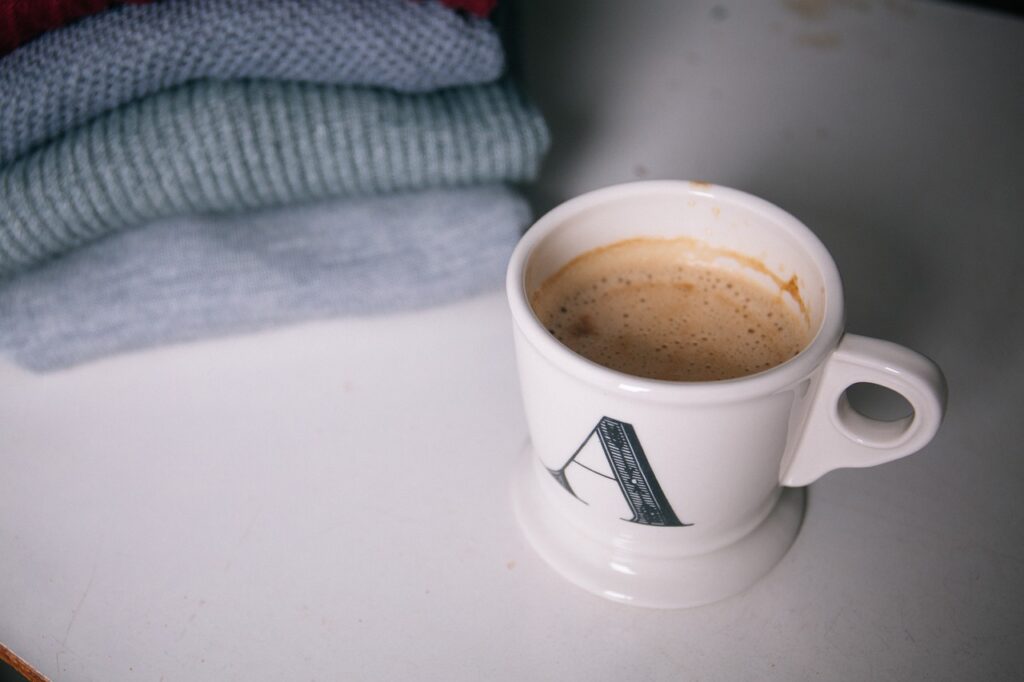 En kopp kaffe står på bordet ved siden av en liten stabel med brettede gensere, og skaper en atmosfære som fremmer Tillit i arbeidslivet.