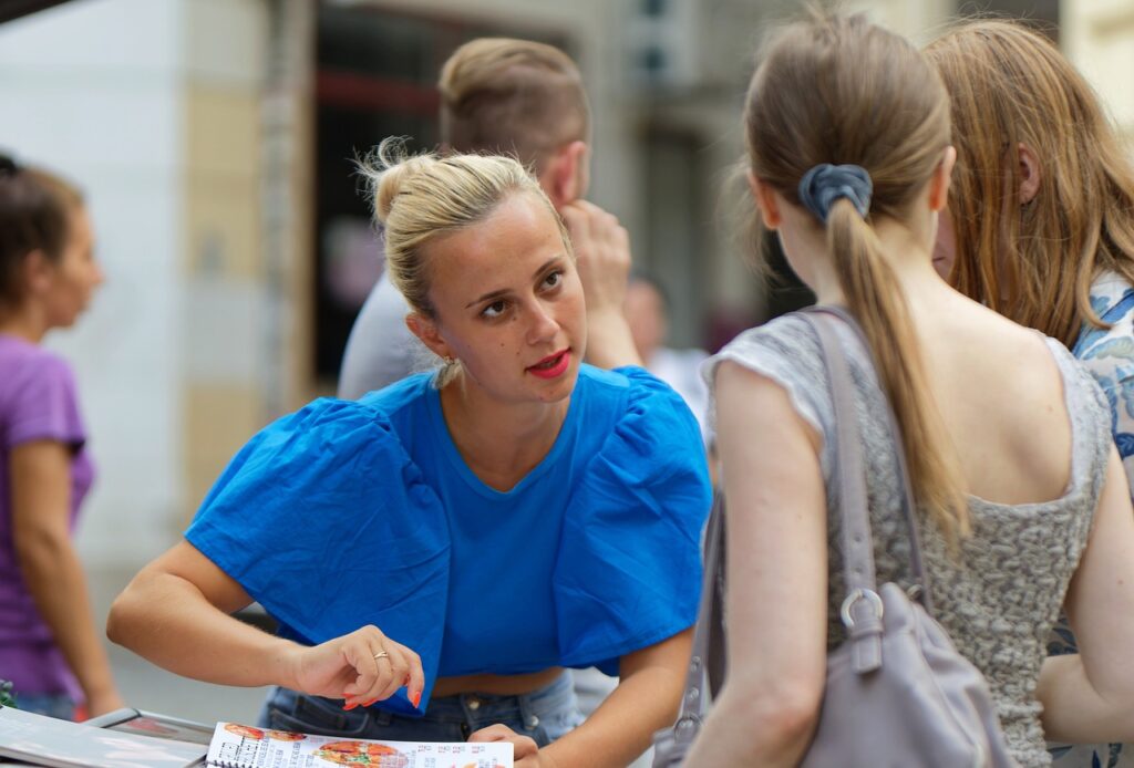 En kvinne i en blå topp snakker med en person i forgrunnen mens hun peker på en bok eller et dokument, og understreker viktigheten av tillit i arbeidslivet.